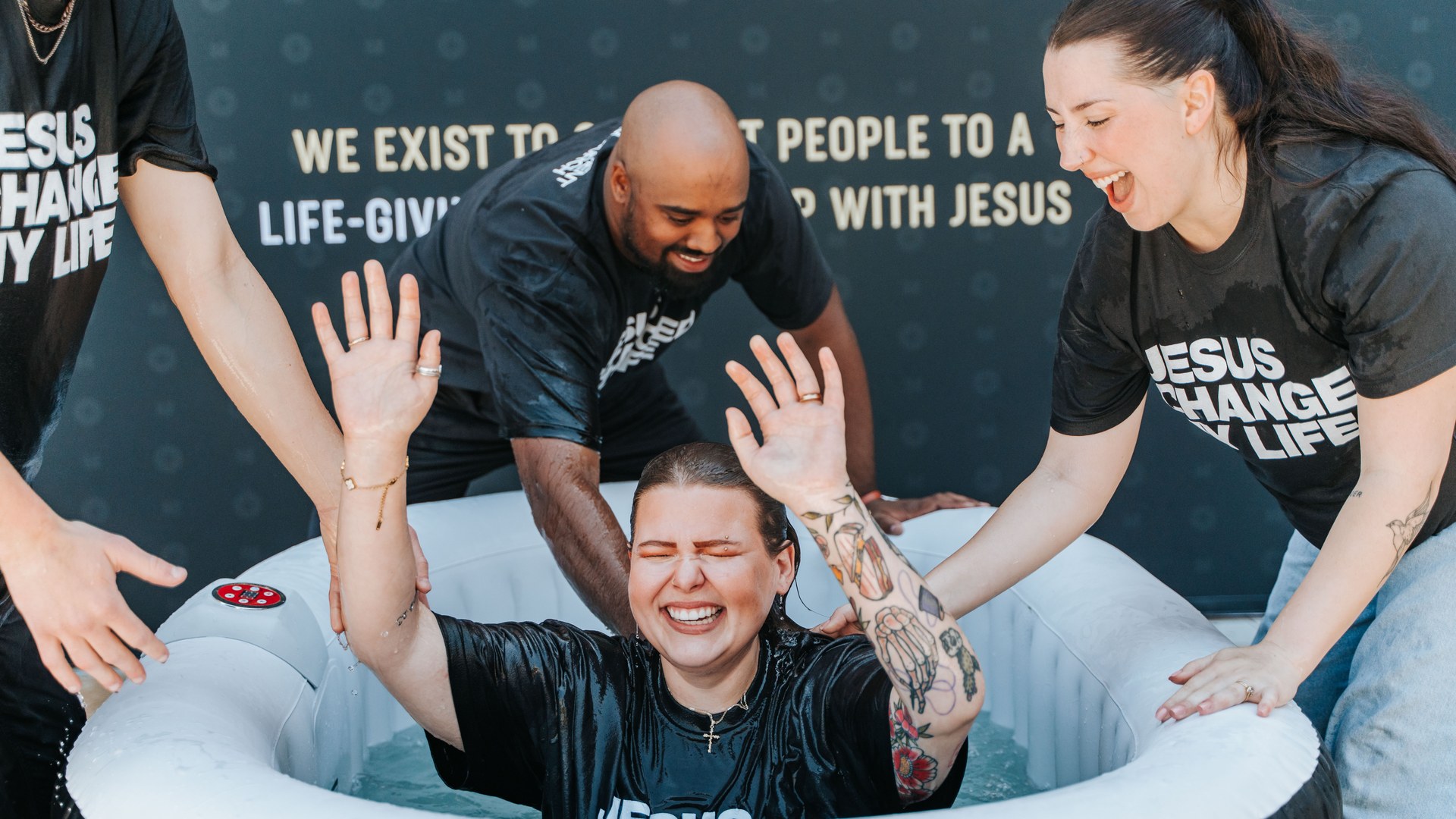 A woman laughing with her hands raised as she comes up out of the water at her baptism at Movement Church, surrounded by a cheering team
